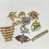 Top down photo of assorted vintage brooches on white background showing detailed designs and variety in styles.