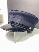 Side angle photo showing the navy blue vintage fire department hat with black patent leather visor and brass button