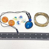 Full view of the vintage jewelry lot with earrings, necklace, bracelet, and buttons on a white background with ruler for scale