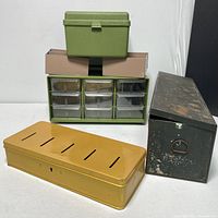 Overall lot view showing various storage containers including the green 9-drawer sorter, green textured box, yellow metal box with slots, and black metal Thermus container.