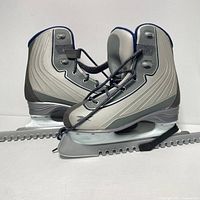 Pair of women's Reebok ice skates displayed side by side, showing gray and white design with blue lining and lace-up closure with ankle strap