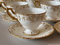 Close-up showing detailed white porcelain tea cup with gold vine pattern and gilded handle
