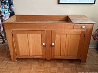 Front view of antique Canadian pine dry sink showing two panel doors with white knob handles, recessed sink surface with backsplash, and drawer on right side.