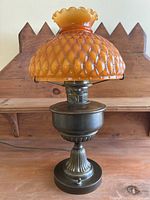 Front view of the antique converted Aladdin oil lamp showing the orange textured glass shade and bronze metal base.