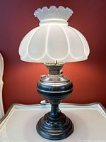 Full view of the antique oil lamp converted to electric with milk glass shade on a white table against a red wall.