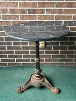 Front view of round grey marble table with decorative cast iron base against brick wall.