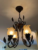 Front view of the hung light fixture showing four lit frosted glass tulip-shaped shades and wrought iron arms with leaf details.