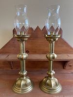 Pair of heavy brass candlesticks with clear glass hurricane shades shown from front.