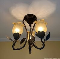 Front view of the 3-arm bronzed metal and glass ceiling light fixture illuminated, showing tulip-shaped frosted glass shades and vine and leaf metal decoration.