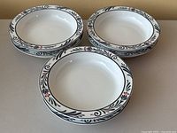Top-down view showing three white ceramic soup or pasta bowls with rimmed decoration in black, green, and red floral and leaf patterns.