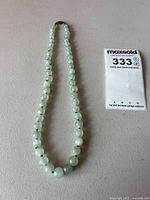 Full view of the pale green jade beaded necklace laid out flat showing overall length and bead size progression.