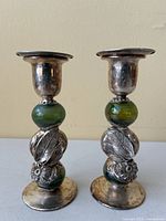 Pair of silver and green art glass candlesticks with floral and leaf designs, showing front view with Hebrew writing on silver tops.