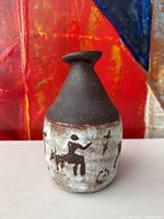 Front view of rustic ceramic bud vase showing matte black top and primitive animal and handprint motifs on whitewashed lower section.
