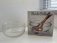 Clear glass salad bowl displayed beside original box packaging showing salad utensils image.