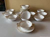 Full set of 12 cream handled soup bowls and 12 saucers arranged with one bowl on saucer front and center, showcasing size and pattern.