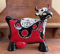 Front and left side view of the ceramic cow sculpture showing black, red, and white folk art patterns and signature artistic details.