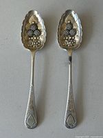 Photo of the full pair of silver serving spoons viewed from above showing the front with berry embossed bowls and decorated handles.