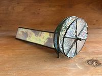 Side view of stained glass kaleidoscope showing iridescent body and floral middle pane with black soldered borders and metal tripod feet.