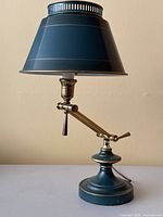 Front view of vintage desk lamp with teal conical shade and brass articulating arm.