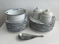 Stacked salad and lunch plates, Maribo baking dish on top, cream and sugar bowls stacked, and spoon rest in front.