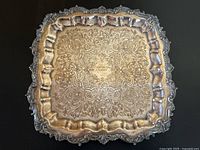 Top-down image showing the ornate floral engraving and Eatons Trophy inscription in center on silver plated tray with tarnish.