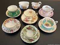 Seven vintage mismatched teacup and saucer sets including one with green Royal Chelsea cup and saucer, plus white creamer and sugar bowl with rose decoration