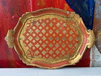 Top-down view of the vintage Florentine wooden tray showing red and gilt diamond motif, ornate edges, and handles with visible wear and paint loss.