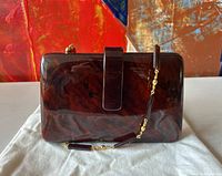 Front view of the purse showing the faux tortoiseshell lucite body, leather flap, and attached gold-tone chain strap with lucite beads.