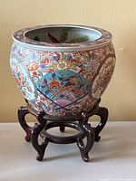 Side view of the painted Asian porcelain jardiniere on the wooden stand showing floral and bird motif on outside surface.