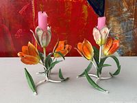 Pair of two toleware floral candleholders together on table against painted backdrop