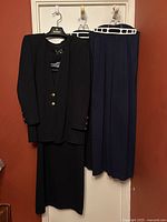 All four garments hanging on door: cardigan, skirt, black pants, navy pants