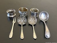 Full lot of six silver items including two napkin rings, two pierced spoons, one fork, and one ladle shown for scale and detail.