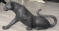 Side view of the crouching black panther statue with white speckles on a light floor.