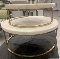 Two stacked round cake stands featuring honed white marble tops and gold electroplated metal bases. Larger stand below and smaller stand nested on top.