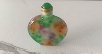 Front view of Chinese natural jade snuff bottle with green, orange, and purple mottled coloration, short neck, and green jade stopper with gold-tone collar.