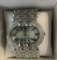 Close-up of Croton watch face and band showing rhodium plating, mother of pearl dial, Roman numerals, and rhinestone embellishments.