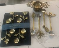 Photo showing the 8 decorative teaspoons with nature-inspired motifs, still attached to original card band with Anthropologie branding.