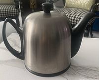 Side angle showing the teapot with stainless steel cover and black porcelain handle and spout.