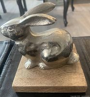Side view of silver bunny figurine on wooden base showing textured ears and body with shiny finish.
