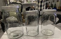 Three clear glass jars with white lids placed on a marble surface, viewed from the front and side showing varying sizes.