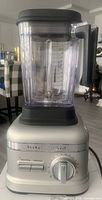 Front view of silver KitchenAid blender with clear plastic jar, black lid and base controls visible
