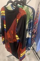 Photo showing colorful long sleeve tops on hangers, highlighting unique print and colors including multicolor patchwork and green blue abstract design.
