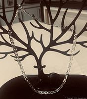 Silver plated necklace displayed on a black decorative holder with branch-like design.