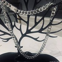 Silver plated chain necklace hanging on black tree-shaped jewelry stand, showing length and clasp