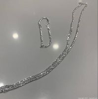 Necklace and bracelet laid flat on a white surface showing length and link design.