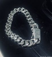 Close-up photo of the sterling silver Cuban link bracelet laid in a loop, showing the box clasp with .925 hallmark.