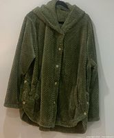 Front view of the green faux fur hooded jacket hanging on a hanger with button closure and front pocket details.