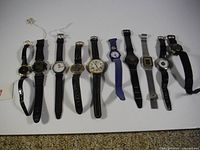 Front view of 10 assorted wrist watches laid out in a row, showing variety of styles and strap materials.