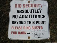 Full view of a square metal sign with text in black and red on white background, slightly worn and rusted around mounting holes, featuring a pig cartoon.