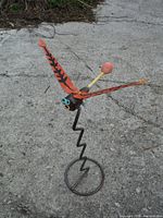 Photo showing the garden sculpture from an angled side view on a concrete ground, highlighting orange wings and spiral base.